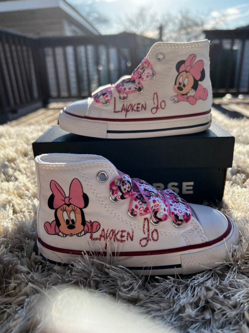 May include: White high-top sneakers with pink Minnie Mouse characters and the name "Layken Jo" written in pink glitter.