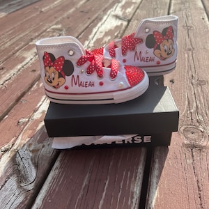 Peut inclure: Baskets montantes blanches avec un motif Minnie Mouse, des n&oelig;uds et des accents &agrave; pois rouges. Le nom "MALEAH" est imprim&eacute; sur le c&ocirc;t&eacute;. Les chaussures sont orn&eacute;es de strass rouges et de lacets &agrave; pois rouges. Les chaussures sont sur une bo&icirc;te noire.