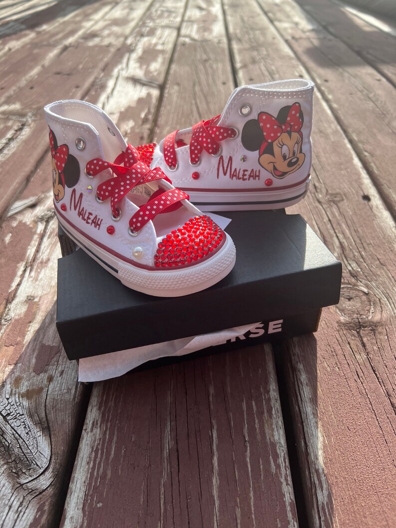 Peut inclure: Baskets montantes blanches avec des lacets rouges &agrave; pois et des motifs de Minnie Mouse. Les bouts des chaussures sont orn&eacute;s de strass rouges. Le nom "Maleah" est imprim&eacute; sur le c&ocirc;t&eacute; de chaque chaussure. Les chaussures sont pr&eacute;sent&eacute;es sur une bo&icirc;te Converse noire.