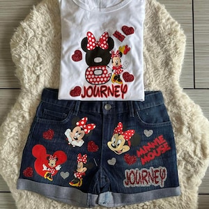 Peut inclure: Ensemble compos&eacute; d'un t-shirt blanc et d'un short en jean avec des motifs de Minnie Mouse. Le t-shirt pr&eacute;sente un grand motif de Minnie Mouse et le mot "JOURNEY". Le short en jean affiche &eacute;galement des images de Minnie Mouse et les mots "MINNIE MOUSE" et "JOURNEY".