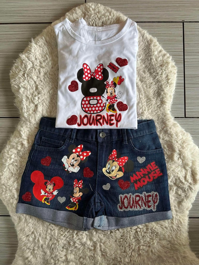 Peut inclure: Ensemble compos&eacute; d'un t-shirt blanc et d'un short en jean avec des motifs de Minnie Mouse. Le t-shirt pr&eacute;sente un grand motif de Minnie Mouse et le mot "JOURNEY". Le short en jean affiche &eacute;galement des images de Minnie Mouse et les mots "MINNIE MOUSE" et "JOURNEY".