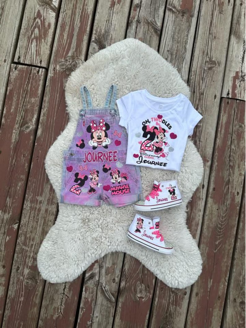 May include: A set featuring pink and blue denim overalls with Minnie Mouse graphics and the name Journee, a white t-shirt with the text Oh Twodles and Birthday Girl Journee, and two white high-top sneakers with pink laces and Minnie Mouse designs.