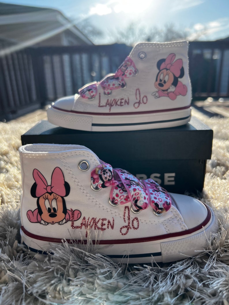 May include: White high-top sneakers with pink Minnie Mouse characters and the name "Layken Jo" written in pink glitter.