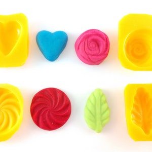 May include: Six silicone molds for making candy or chocolate. The molds are yellow and feature different shapes, including a heart, a rose, a swirl, a leaf, and a shell.