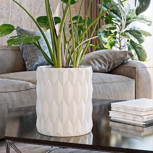 May include: White geometric planter with a green plant inside. The planter is sitting on a dark brown coffee table.