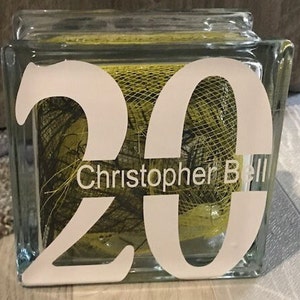 Puede incluir: Un bloque de vidrio con el número 20 impreso en blanco. El bloque está lleno de red amarilla y verde y el texto "Christopher Bell" está impreso debajo del número.