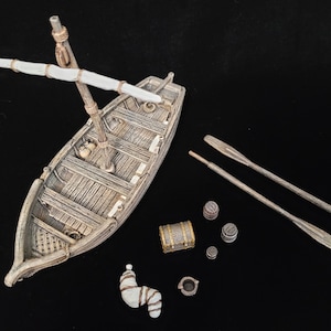 May include: A detailed miniature wooden boat with a mast and sail, accompanied by oars, barrels, a treasure chest, and other nautical accessories. The boat and accessories are painted in shades of brown and beige.