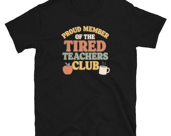 Könnte beinhalten: Schwarzes T-Shirt mit Retro-Design. Das Design enthält den Text "PROUD MEMBER OF THE TIRED TEACHERS CLUB" in Orange, Gelb und Grün. Ein Apfel und eine Kaffeetasse sind ebenfalls abgebildet.