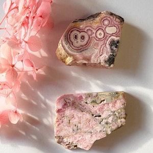 May include: Two pink and white polished pieces of  pink  opalite, a popular crystal for healing and meditation. The first piece has a swirling pattern, while the second piece has a layered pattern.