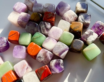 May include: A collection of tumbled gemstone cubes in various colors, including amethyst, green aventurine, tiger's eye, red jasper, and clear quartz.
