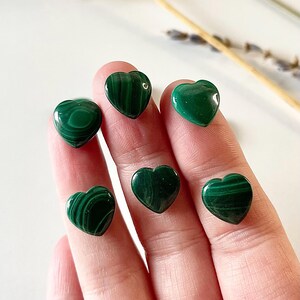 May include: Six green malachite heart-shaped stones. The stones are smooth and polished, with a swirling pattern of green and black.