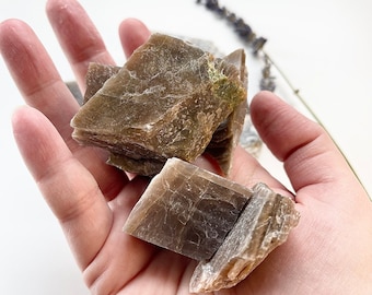 May include: A collection of brown mica mineral specimens with a layered, flaky texture. The mica is arranged in a pile, showing its natural, raw form.