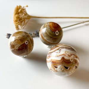 May include: Three polished onyx spheres with brown and white swirling patterns. The spheres are displayed on a white surface.