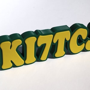 May include: A green and yellow 3D word sign that reads "KITCJ".