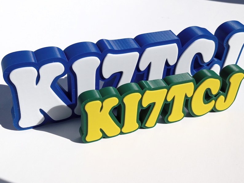May include: Three dimensional letters spelling "KITCJ" in blue, white, green, and yellow. The letters are stacked on top of each other.