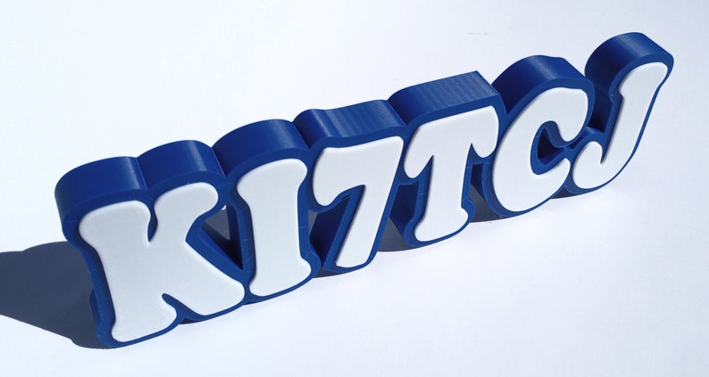 May include: A blue 3D-printed sign with the word "KITCJ" in white letters.