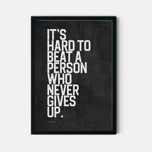 Peut inclure: Une affiche encadrée avec un fond gris anthracite foncé et une police blanche texturée à l'aspect vieilli. Le texte indique : IT'S HARD TO BEAT A PERSON WHO NEVER GIVES UP. Le nom BABE RUTH est imprimé en plus petit en bas au centre.