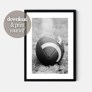Puede incluir: Una impresión de arte mural enmarcada en blanco y negro que muestra un balón de fútbol americano sobre el césped. La imagen incluye el texto download & print yourself. El balón tiene una superficie texturizada con cordones y una franja.
