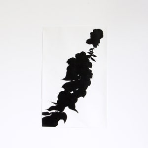 May include: A black floral silhouette print on a white rectangular paper. The artwork features a stylized depiction of a flower stem with leaves and blooms. The contrast between the black design and the white background creates a striking visual.