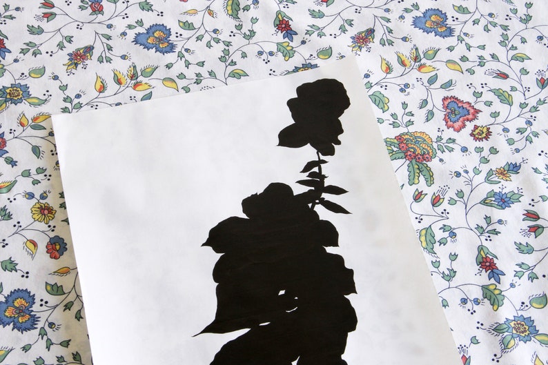 May include: A black silhouette of a rose with leaves and stem on a white background. The floral design is set against a patterned fabric with a white background and colorful flowers.