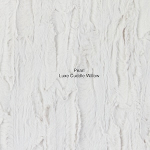 May include: Close-up of a white faux fur fabric with a soft, fluffy texture. The fabric is called "Pearl Luxe Cuddle Willow".