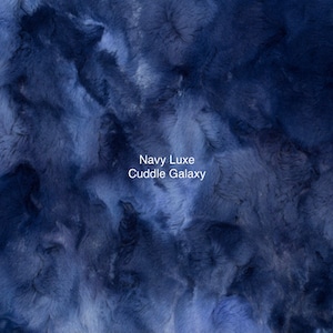 May include: A close-up of a soft, plush fabric in a deep navy blue color. The fabric has a fuzzy, cloud-like texture. The text "Navy Luxe Cuddle Galaxy" is printed in white on the fabric.