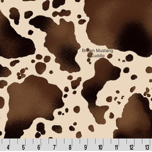 May include: Brown and white cowhide fabric with a brown and white spotted pattern. The fabric has the text "Brown Mustang Cuddle" printed on it.
