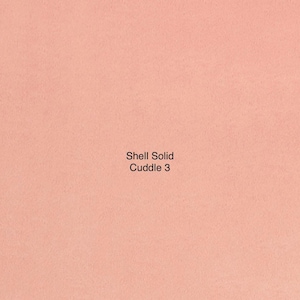 May include: A solid, peach-colored fabric with a soft, textured appearance. The text "Shell Solid Cuddle 3" is printed in the center. This fabric is likely used for blankets, throws, or other cozy items.