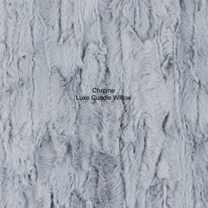 May include: Close-up of a soft, light blue faux fur fabric with a textured, wavy pattern. The fabric is labeled "Chrome Luxe Cuddle Willow."