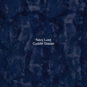 May include: A close-up of a navy blue faux fur fabric with the text "Navy Luxe Cuddle Glacier" printed on it.