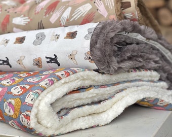Pode incluir: Uma pilha de três camas para animais de estimação com diferentes tecidos estampados. A cama superior tem um fundo bege com ilustrações de mãos. A cama do meio tem um fundo branco com ilustrações de cães. A cama inferior tem um fundo azul com ilustrações de rostos de desenhos animados.
