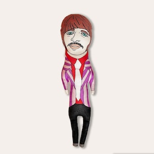 May include: A handmade plush doll of a person with brown hair, a purple and pink striped jacket, a red shirt, and a black tie. The doll has a painted face with brown eyes, a moustache, and a light brown beard.