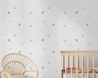 May include: A white wall with a gray watercolor dot pattern. A wooden crib with a white mattress and a gray and yellow blanket is in the foreground. A wicker chair with a light brown cushion is in the foreground. The text "WEST COAST WALLS" is in the lower left corner of the image.
