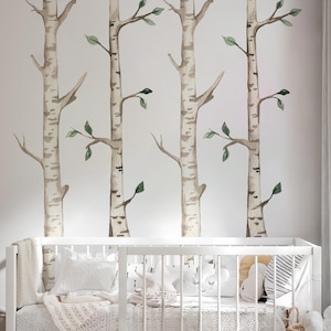 May include: A white cot with a white and black patterned sheet and a white blanket. The cot is in a room with a white wall and a birch tree wall decal. There is a woven basket with white towels next to the cot.