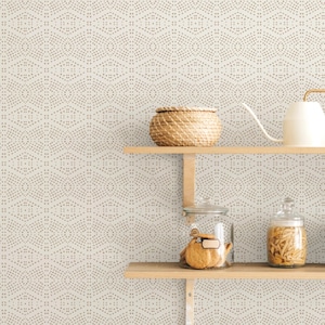 May include: A kitchen scene in neutral tones, with two wooden shelves against patterned wallpaper. The top shelf has a woven basket and a white watering can. The lower shelf displays glass jars with cookies and pasta.