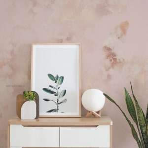 Può includere: Una cassettiera bianca con due cassetti e due ante, una stampa incorniciata di una pianta verde, una lampada lunare bianca e una pianta di serpente in vaso davanti a una parete testurizzata rosa e oro. Il testo 'WEST COAST WALLS' è visibile nell'angolo inferiore sinistro dell'immagine.