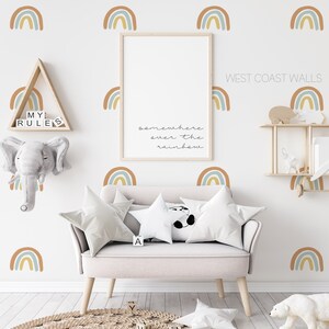 May include: A nursery room with a white wall decorated with rainbow decals. The text "somewhere over the rainbow" is written on the wall. There is a white couch with two pillows and a white stuffed panda bear. There is a wooden shelf with a stuffed animal and a wooden triangle shelf with the text "My Rules".