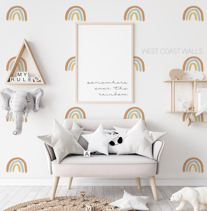 May include: A nursery room with a white wall decorated with rainbow decals. The text "somewhere over the rainbow" is written on the wall. There is a white couch with two pillows and a white stuffed panda bear. There is a wooden shelf with a stuffed animal and a wooden triangle shelf with the text "My Rules".