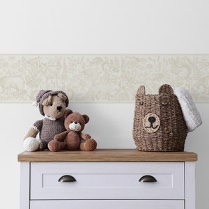 May include: A white dresser with a brown top and two drawers. The dresser has two silver knobs. On top of the dresser are three stuffed animals: a brown bear, a grey bear, and a brown and grey bear. There is also a brown wicker basket with a bear face on the front. The wall behind the dresser has a beige wallpaper border with a white background and a pattern of animals and plants.