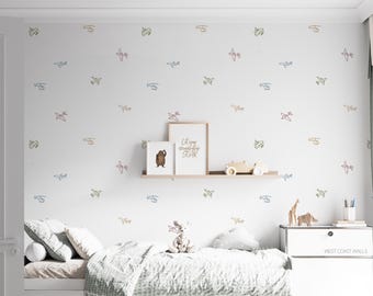 May include: A white bedroom wall decorated with colorful airplane and helicopter outlines. A shelf holds framed art, a wooden car, and decorative items. A bed with pillows and a comforter is in the foreground. The text on the wall art says "Let your imagination soar".