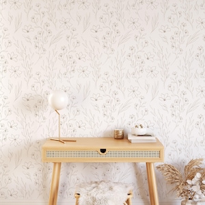 Peut inclure: Une pièce lumineuse avec du papier peint floral, un bureau en bois et un petit tabouret. Une lampe blanche et des objets décoratifs sont posés sur le bureau. Un vase avec des fleurs séchées est au sol. La pièce a une esthétique minimaliste et bohème.