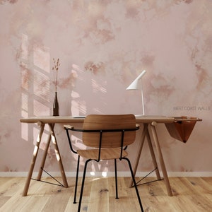 Può includere: Un muro rosa chiaro con un effetto marmoreo sottile, con una scrivania in legno e una sedia in metallo nero. La scrivania ha una borsa di pelle appesa sul lato e una lampada a destra. La stanza ha un pavimento in legno chiaro.