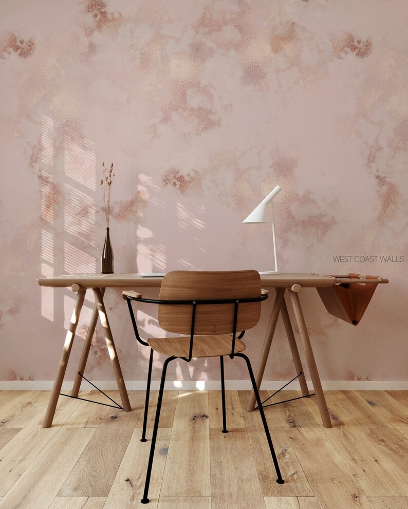 Può includere: Un muro rosa chiaro con un effetto marmoreo sottile, con una scrivania in legno e una sedia in metallo nero. La scrivania ha una borsa di pelle appesa sul lato e una lampada a destra. La stanza ha un pavimento in legno chiaro.