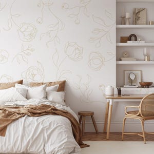 Può includere: Una camera da letto con un letto con lenzuola bianche e una coperta marrone. La parete è decorata con un motivo floreale dorato. Un piccolo sgabello in legno e una scrivania con una sedia in rattan creano un'atmosfera accogliente.