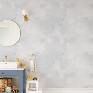 May include: A bathroom with a light blue and white watercolor wallpaper featuring a cloud pattern. The bathroom has a white sink, a blue cabinet, and a white stool with a yellow rubber ducky on top.