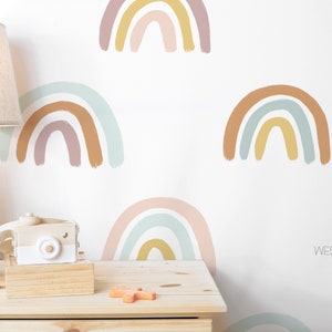 May include: A white wall with a repeating pattern of colorful rainbow decals. The rainbows are painted in shades of pink, blue, yellow, and brown. The wall is decorated with a wooden lamp, a wooden camera, and a wooden block that says "NICE".