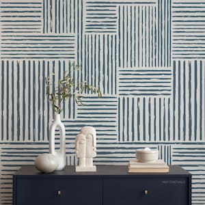 May include: A navy blue and off-white geometric wallpaper pattern with horizontal and vertical brushstroke lines. A dark blue cabinet displays a white vase, a sculpture, and books. The text "WEST COAST WALLS" is visible on the cabinet.