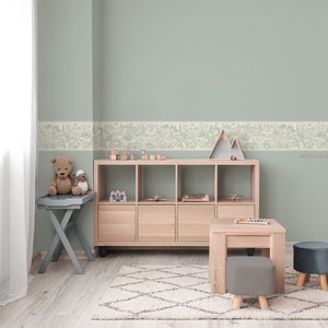 May include: A light green wall with a white border featuring a woodland animal print. A wooden shelf unit with toys and a stuffed animal on a small table are in front of the wall. The text "West Coast Walls" is visible in the bottom right corner of the image.
