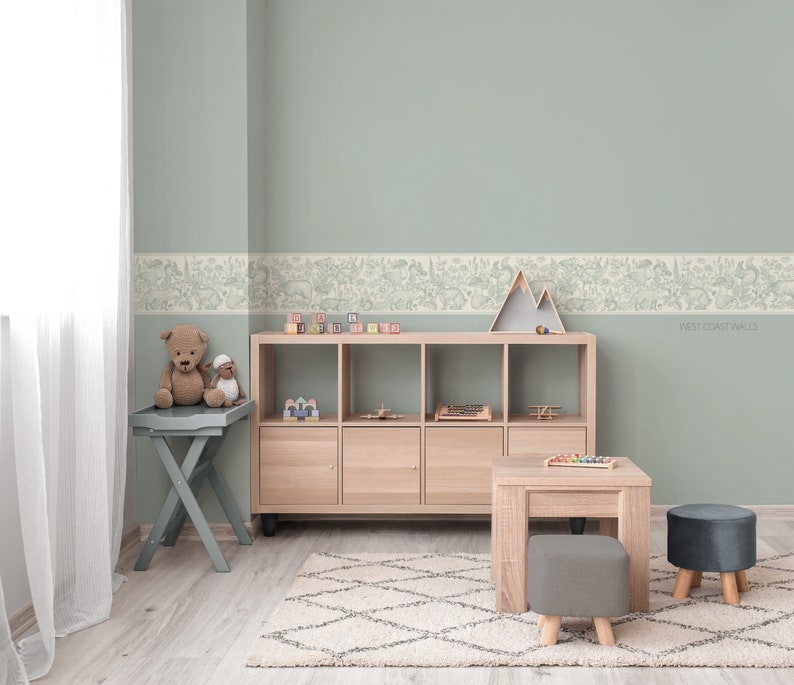 May include: A light green wall with a white border featuring a woodland animal print. A wooden shelf unit with toys and a stuffed animal on a small table are in front of the wall. The text "West Coast Walls" is visible in the bottom right corner of the image.