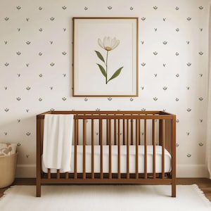 May include: A wooden cot with a white blanket inside, set against a wall with a floral pattern wallpaper. A framed picture of a white flower is hanging on the wall above the cot.